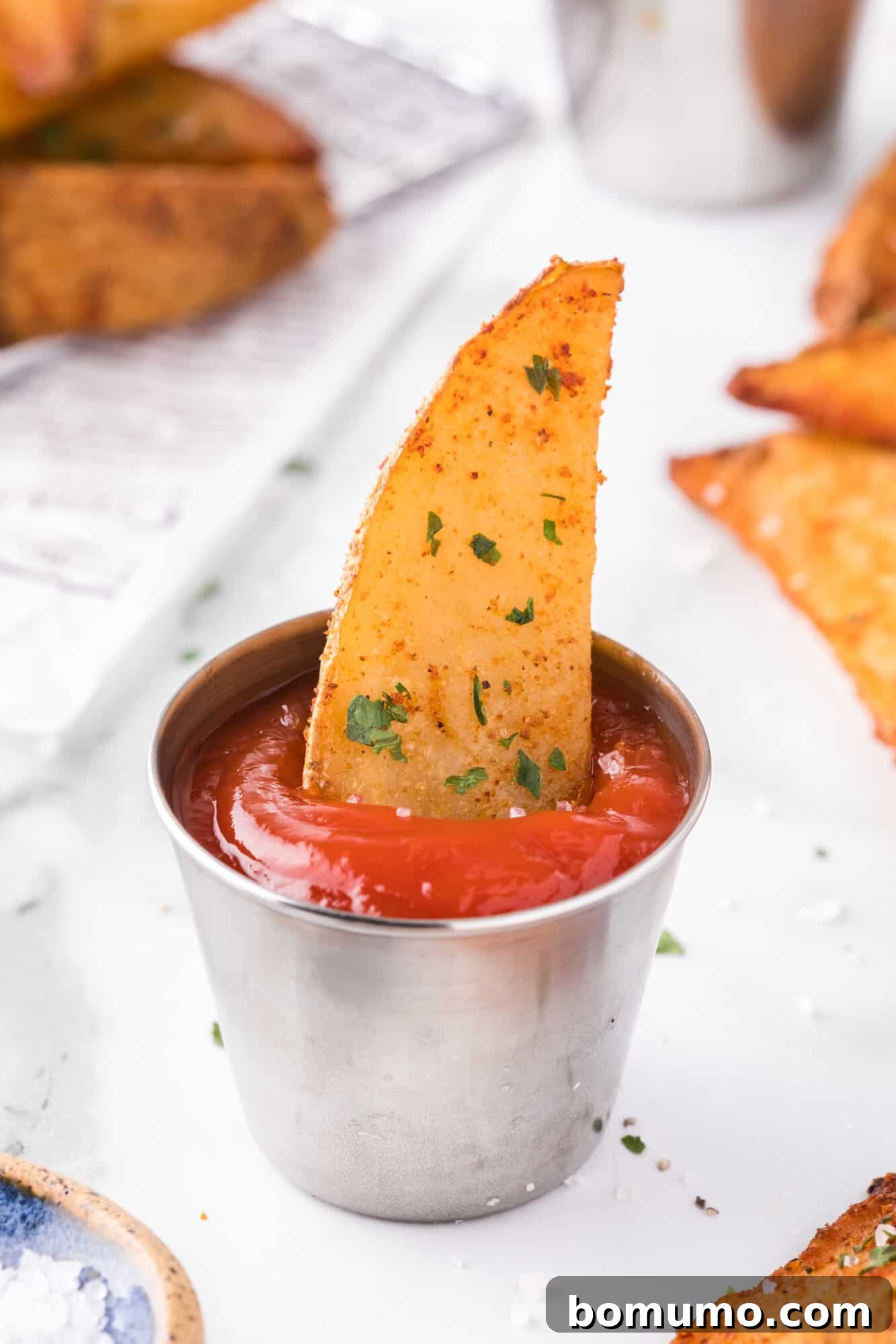 A single crispy potato wedge dipped in a small cup of ketchup, ready to eat.