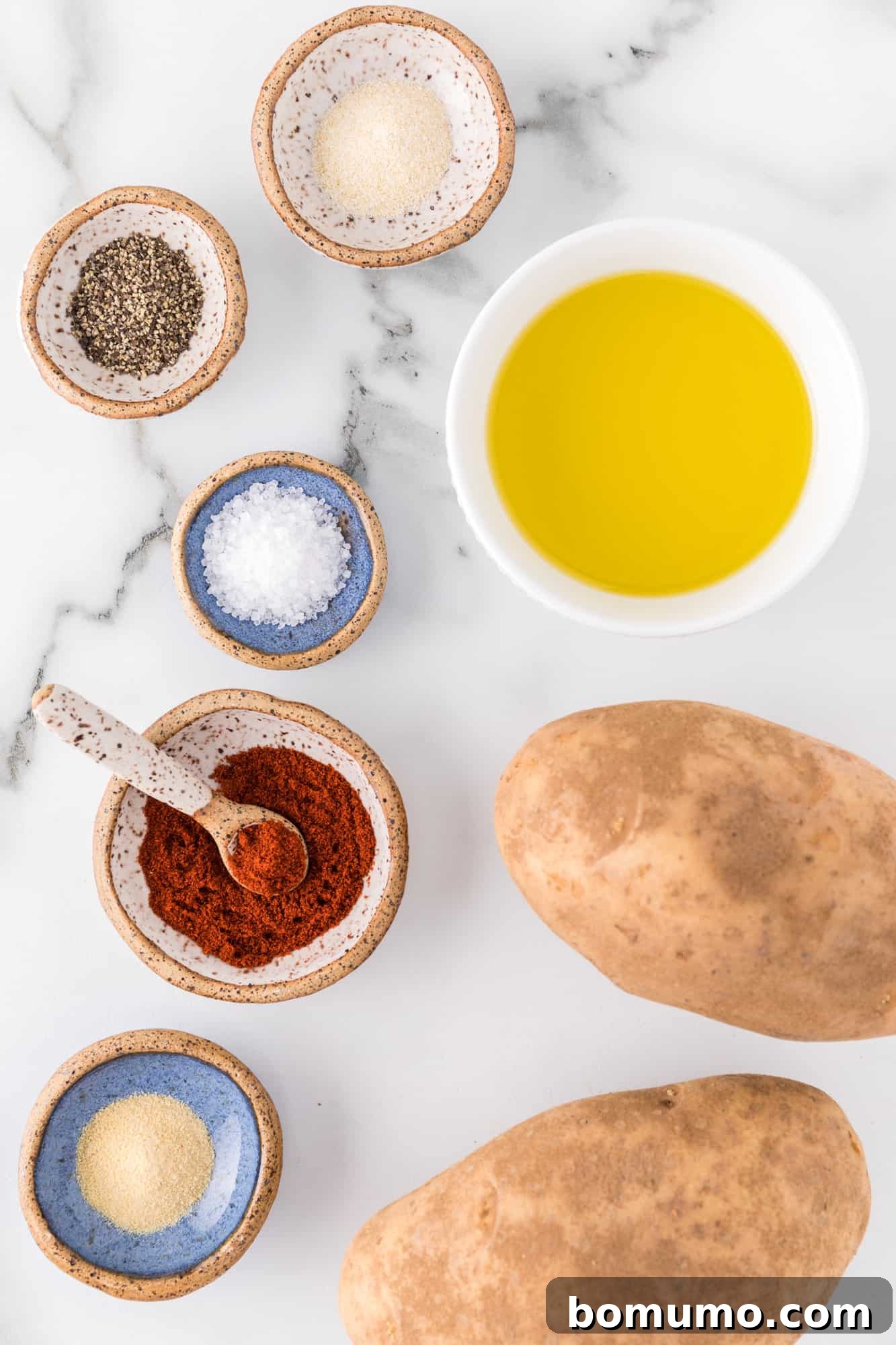Ingredients for air fryer potato wedges laid out: whole potatoes, olive oil, and various spices.