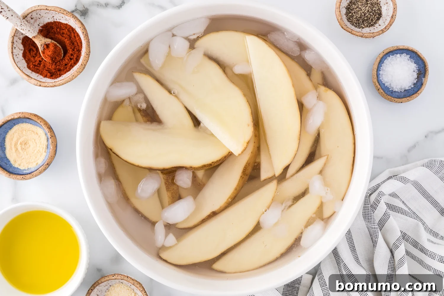 Cut potato wedges submerged in a bowl of cold water, soaking to remove excess starch.