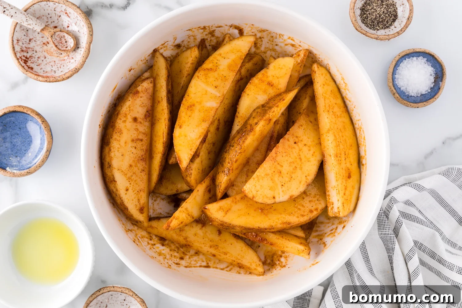 Uncooked potato wedges coated with olive oil and a rich blend of spices, ready for the air fryer.