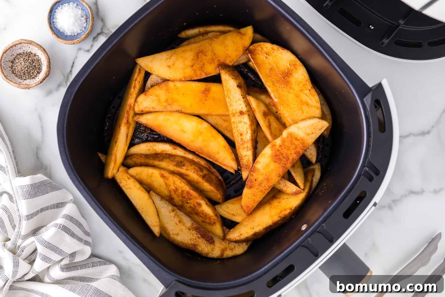 Raw, seasoned potato wedges neatly arranged in a single layer inside an air fryer basket, ready to cook.