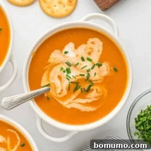 Carrot soup in a white bowl topped with chives and a swirl of cream, for a visually appealing presentation.