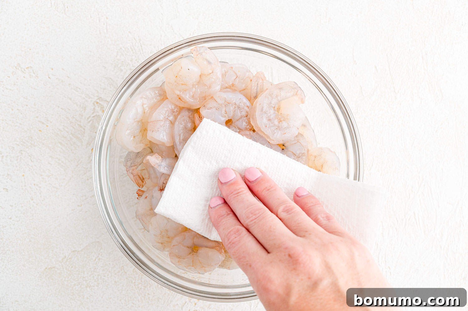 Thawed shrimp being patted dry with paper towels to remove excess moisture.