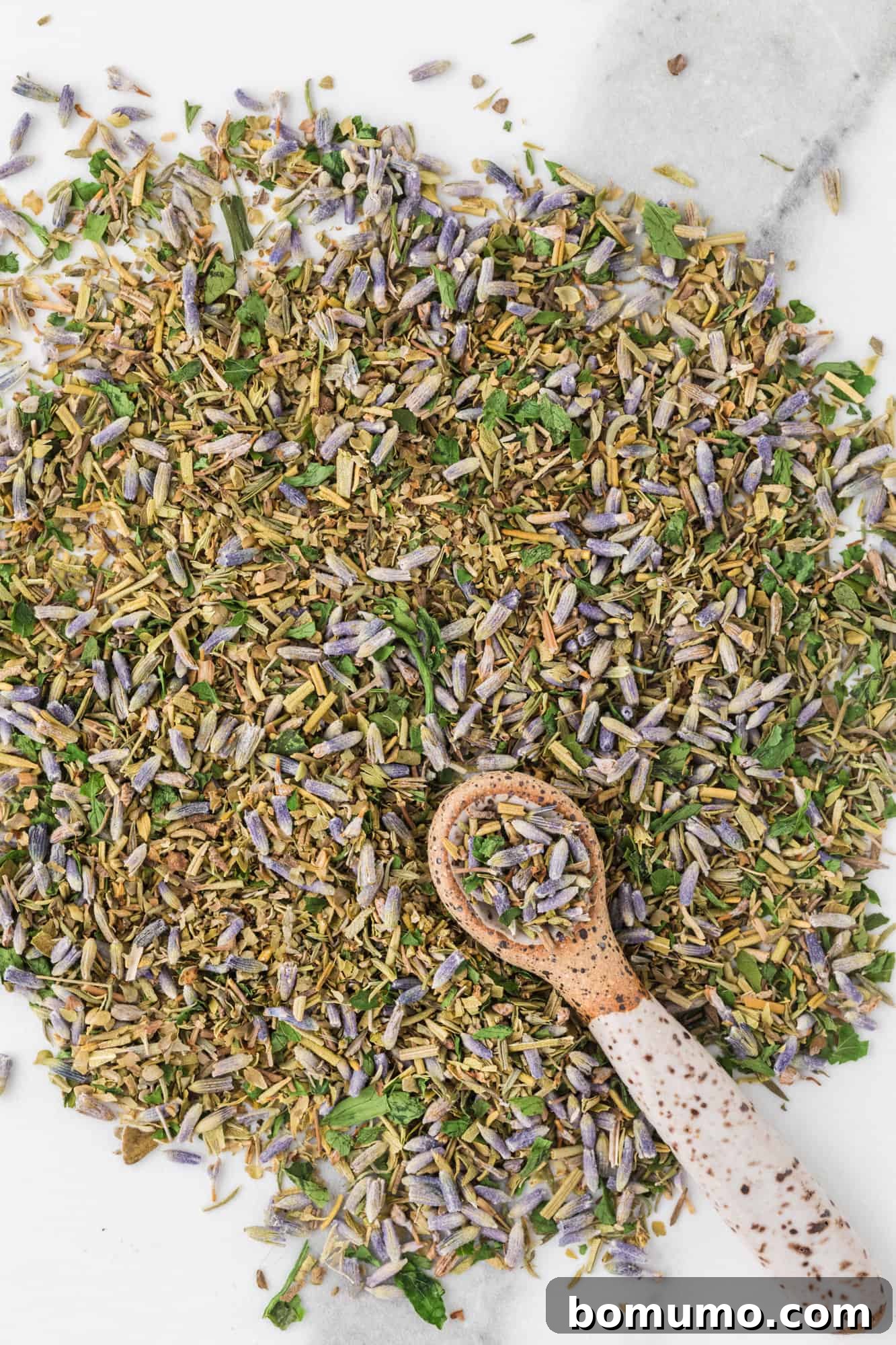 A selection of dried herbs, including thyme, rosemary, and savory, artfully spread on a marble backdrop, highlighting their individual textures and colors.