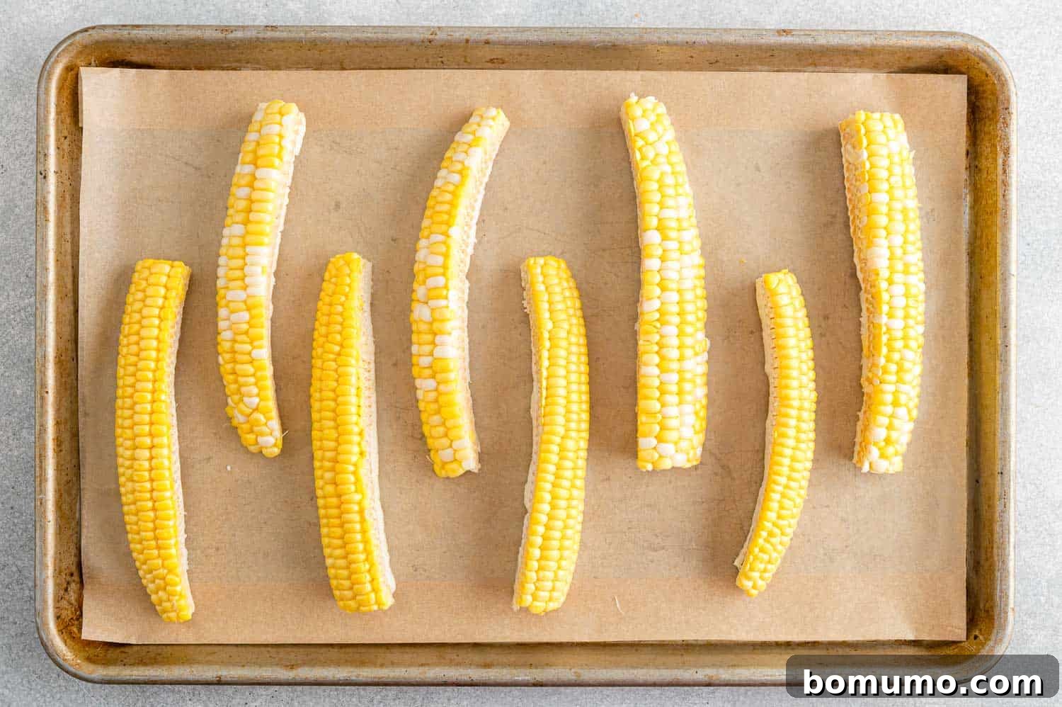 Unseasoned, uncooked corn ribs arranged on a parchment paper lined sheet pan, ready for seasoning.