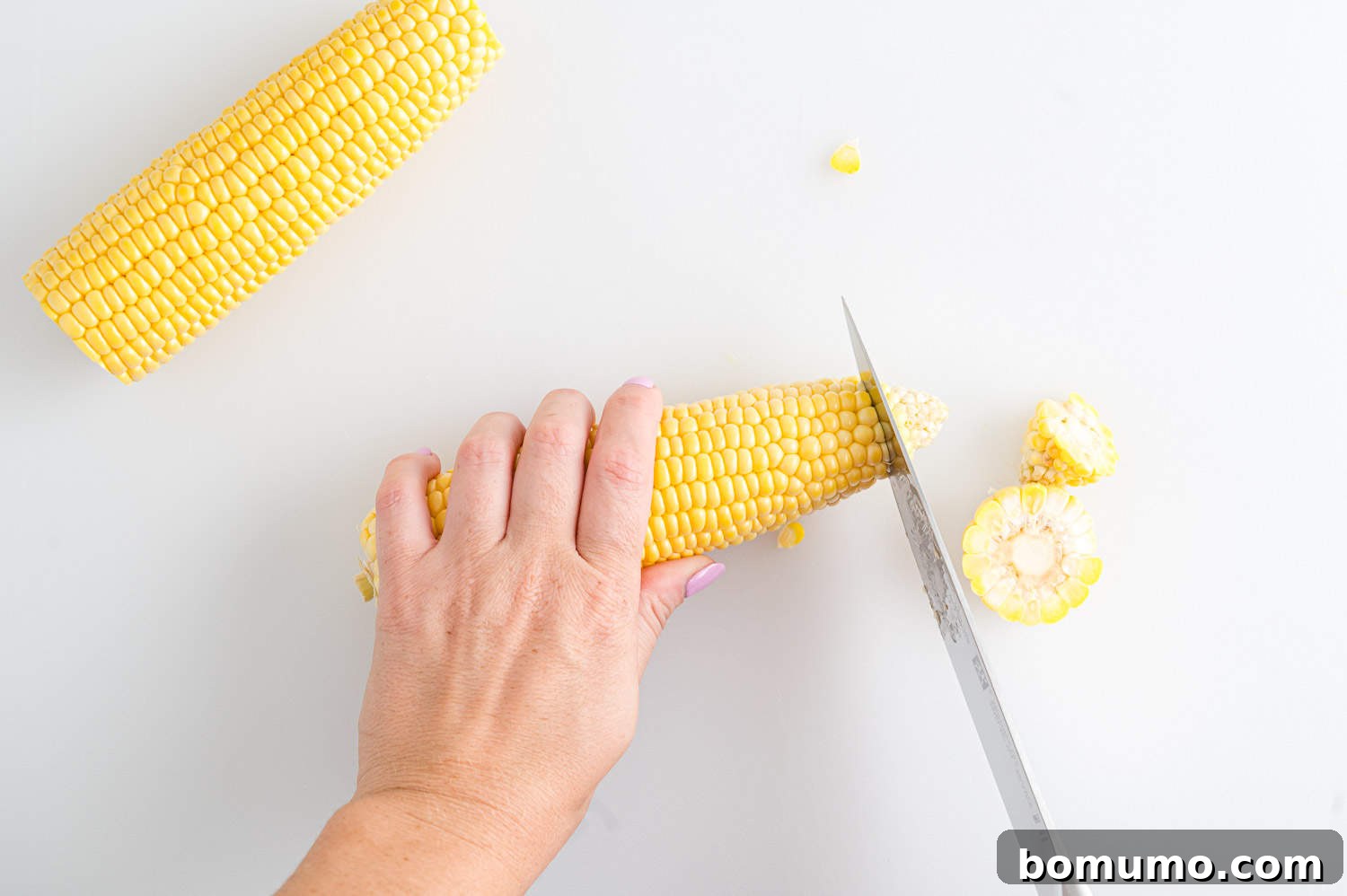 Ends of ear of corn being sliced off to create flat surfaces for stable cutting.