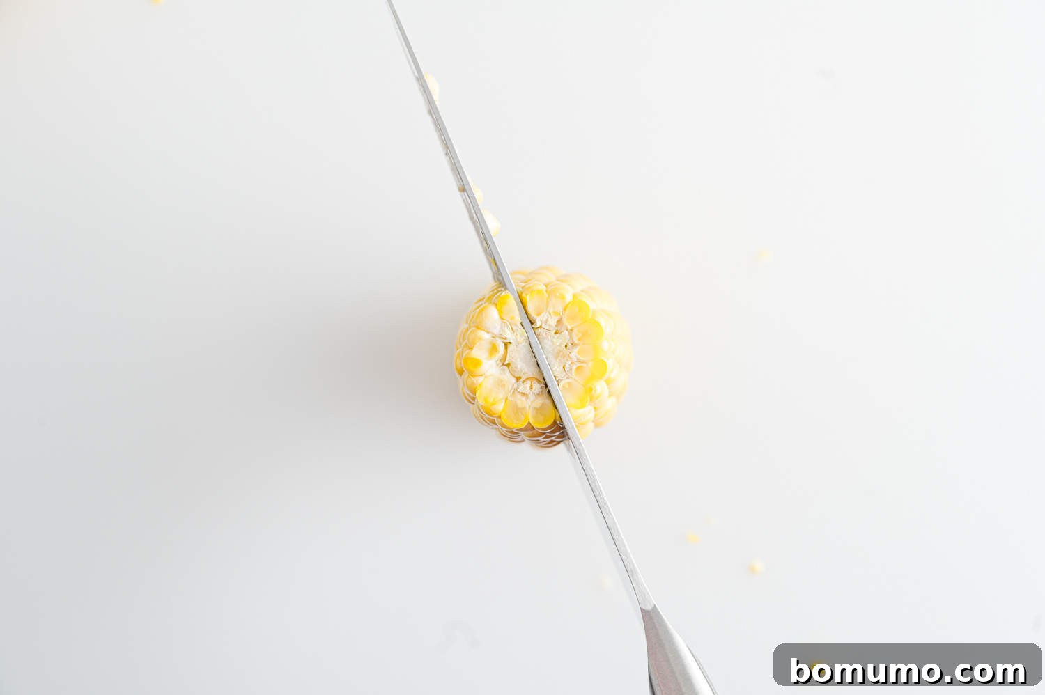 Ear of corn being carefully cut in half lengthwise through the cob using a sharp knife.