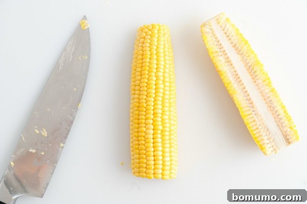 A corn cob sliced in half lengthwise, demonstrating the first cut, with a large knife beside it.