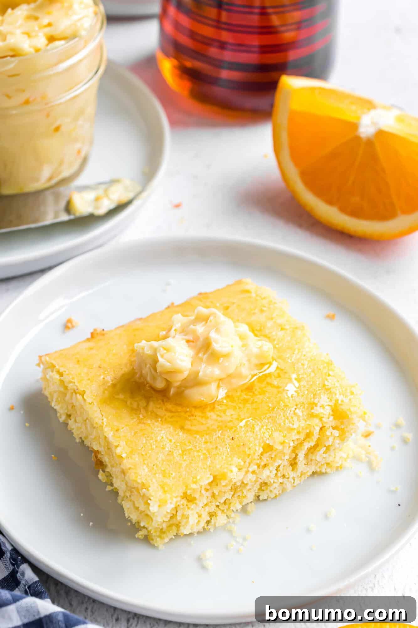 A golden square of cornbread generously topped with luscious orange honey butter, showcasing its creamy texture and inviting color.