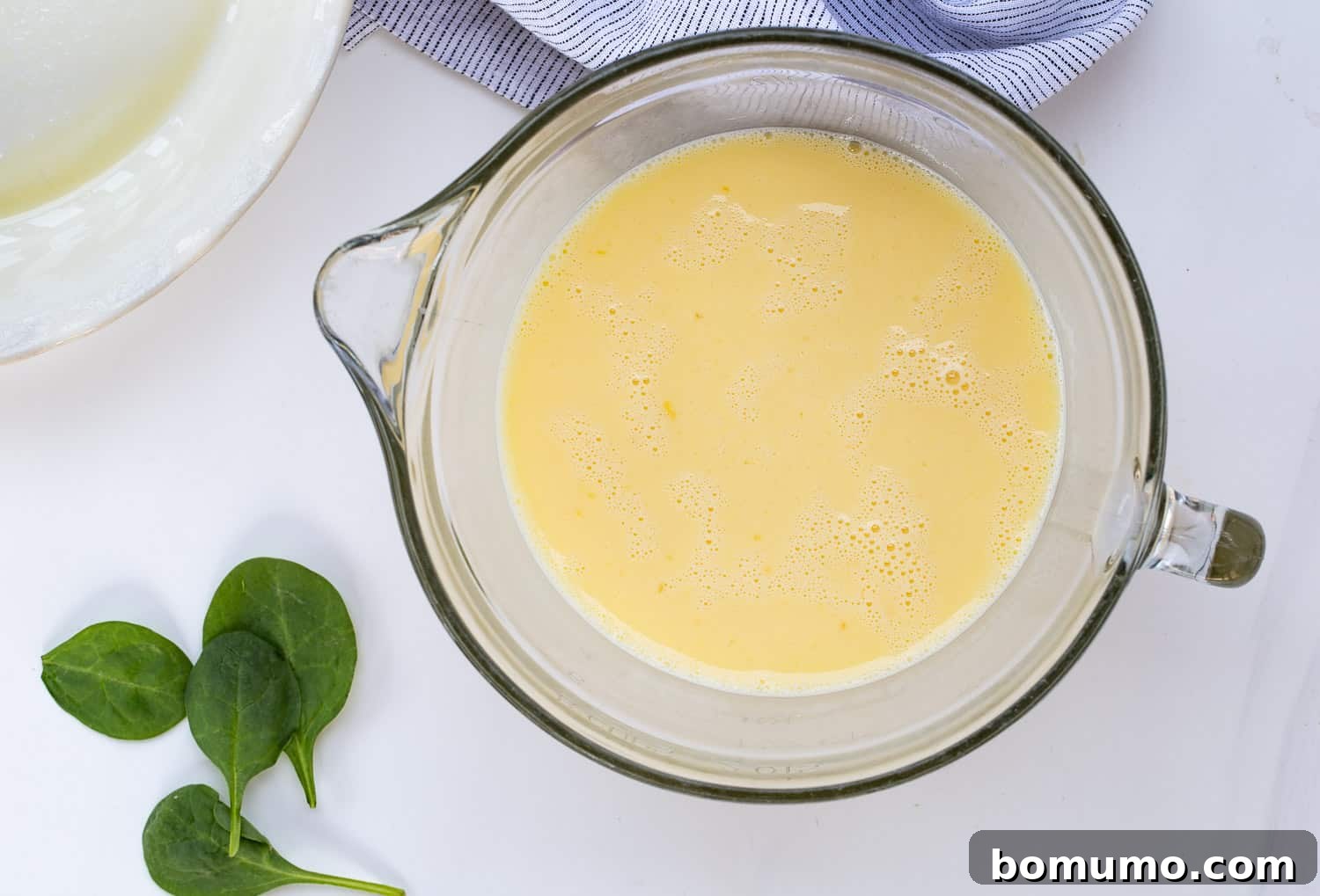 The same mixing bowl, now with the eggs and milk thoroughly whisked together into a smooth, pale yellow, homogenous mixture, ready for seasoning.