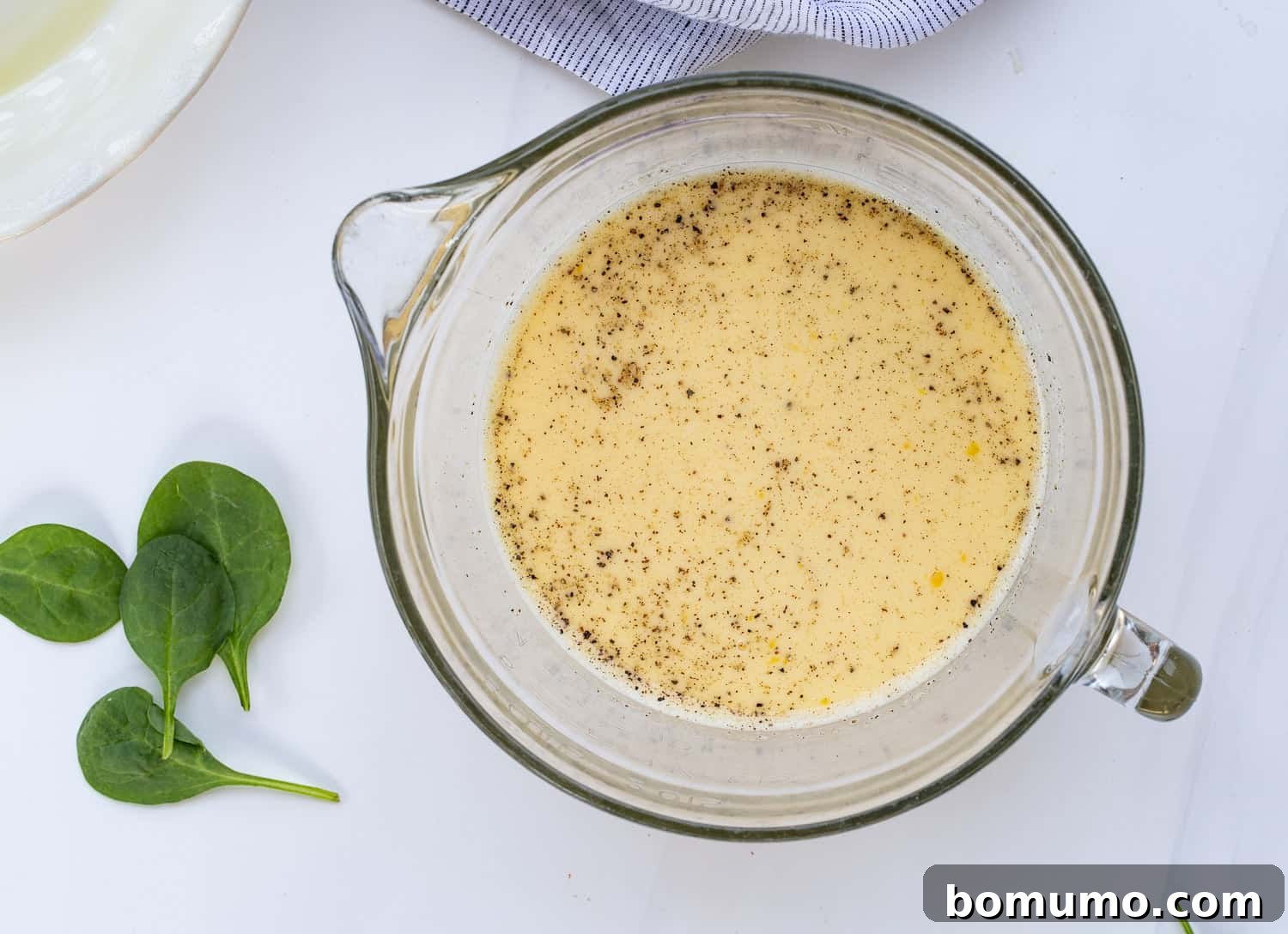 The whisked egg and milk mixture, with the addition of Dijon mustard, salt, pepper, and a pinch of nutmeg, demonstrating the next step in seasoning the quiche base.