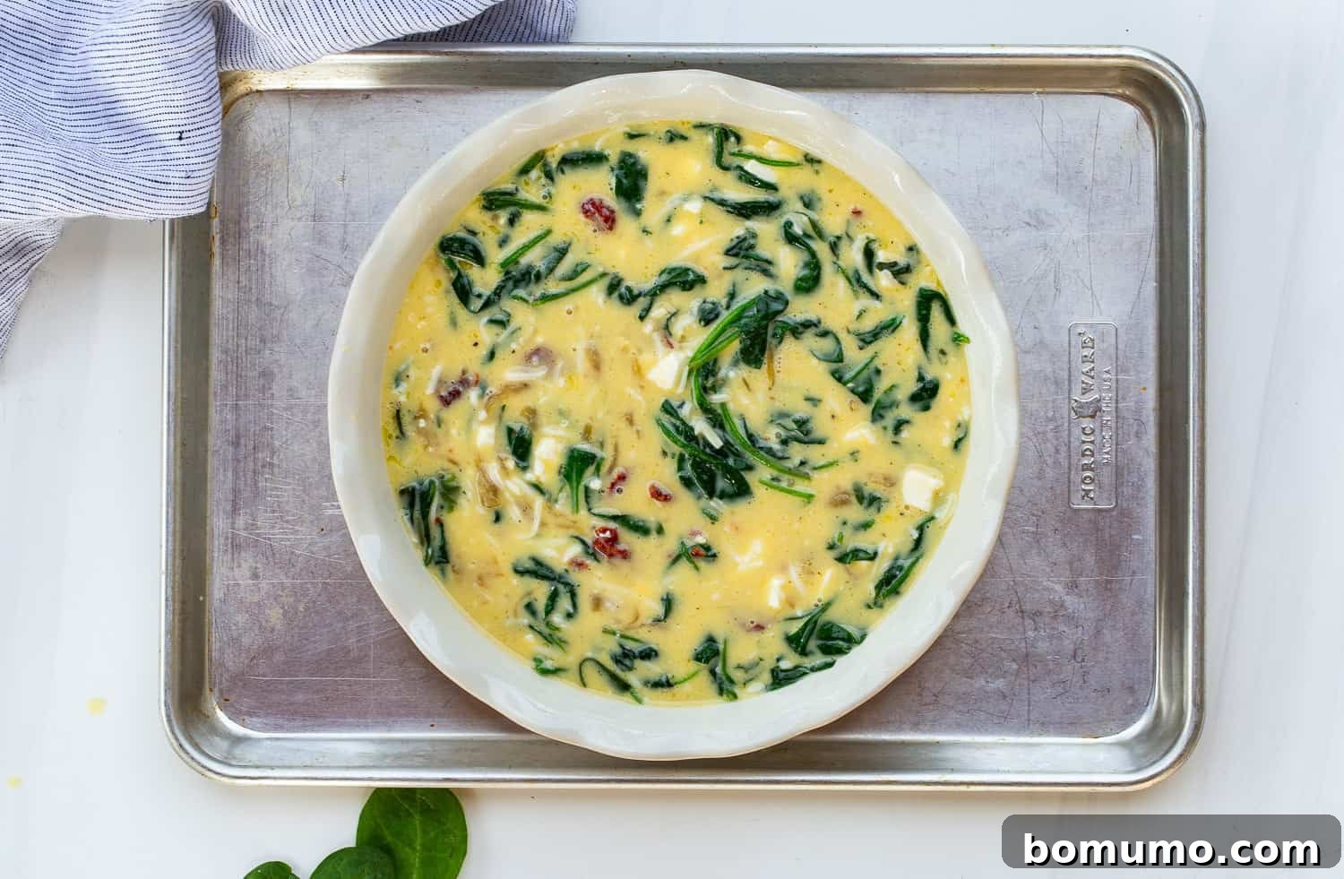 The unbaked crustless quiche mixture poured into a deep-dish pie dish, placed on a rimmed baking sheet ready for the oven, illustrating the safe baking practice.