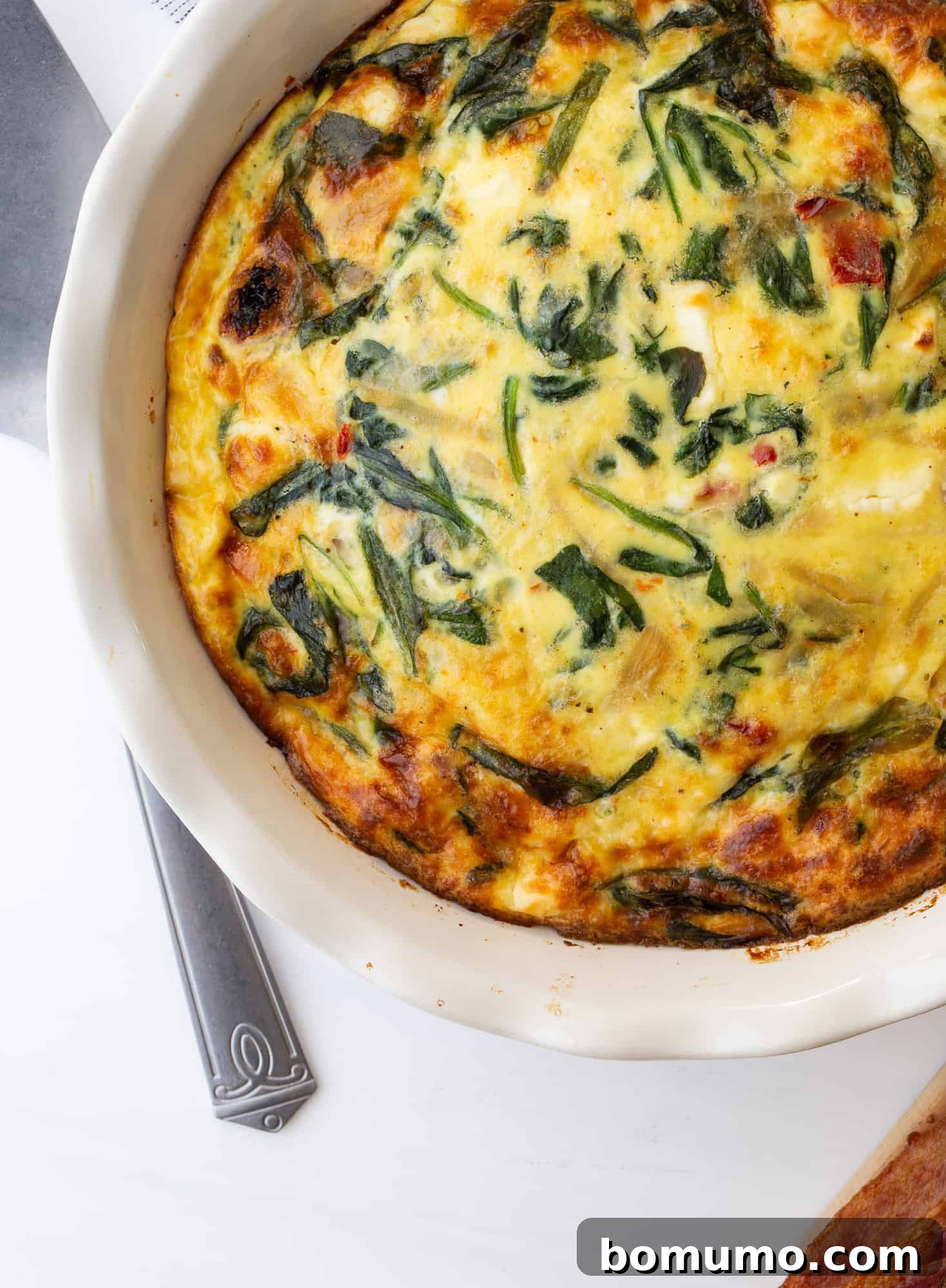 A close-up of the perfectly cooked crustless quiche, showcasing its golden-brown top and the enticing texture of spinach, sun-dried tomatoes, and caramelized onions embedded within.