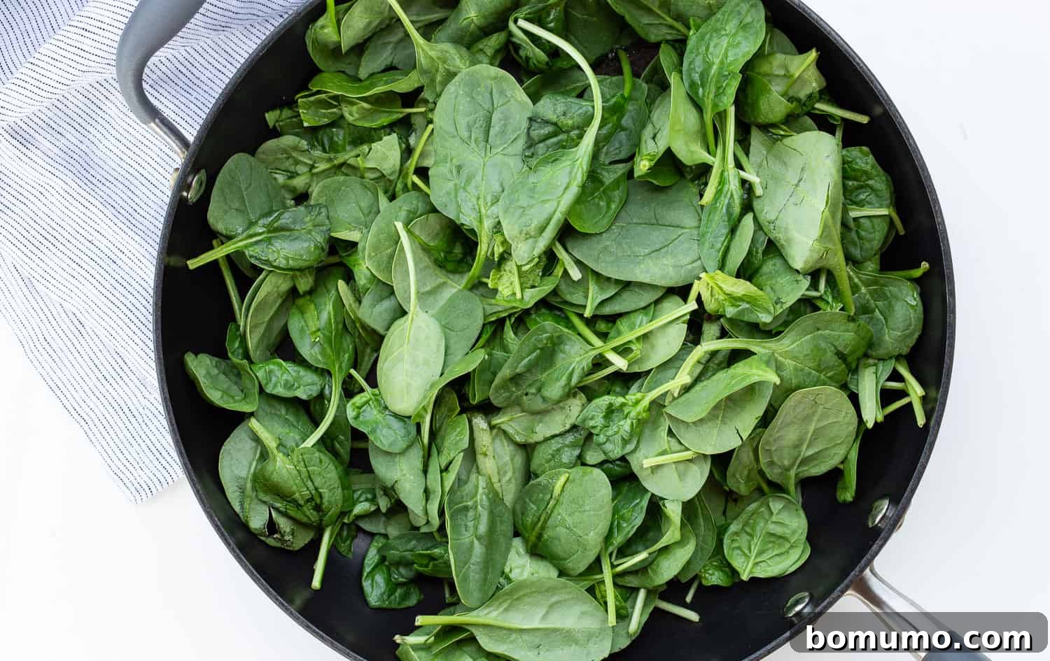 Fresh baby spinach after it has been sautéed and wilted, with any excess liquid removed, showcasing its reduced volume and vibrant green color.