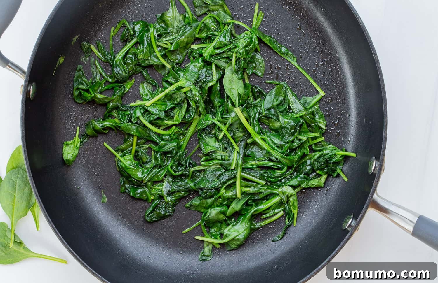 A closer view of sautéed spinach in a colander, with a hand gently pressing down to extract excess water, emphasizing the importance of this step for a perfect quiche texture.