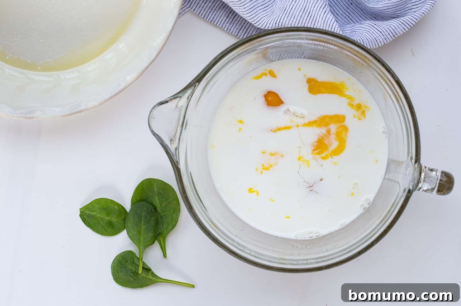 A large mixing bowl containing unmixed eggs and whole milk, showcasing the distinct yellow yolks and white milk before whisking begins.