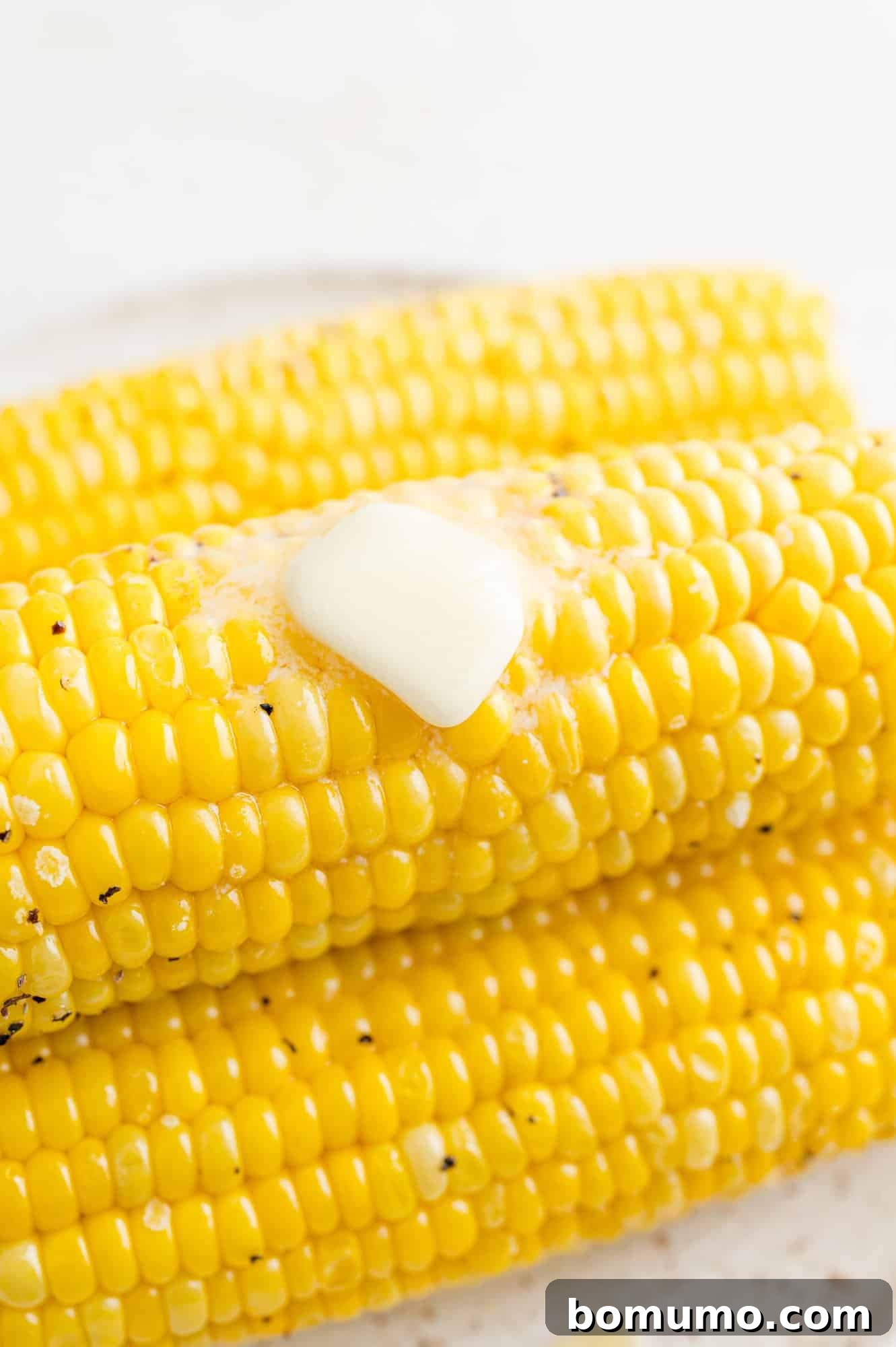Close up of a pat of butter melting over a stack of golden air fryer corn on the cob, perfectly roasted and ready to serve.