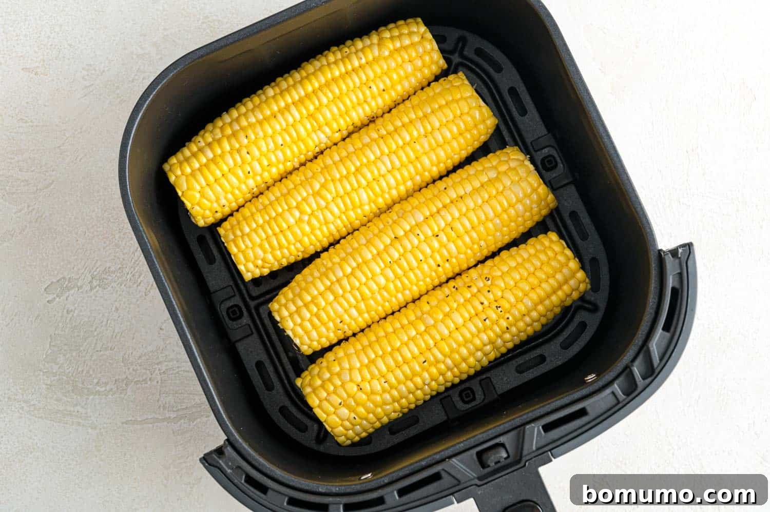 Four ears of corn arranged neatly inside the air fryer basket, ready for cooking.