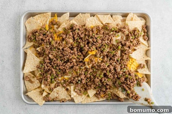 Tortilla chips topped with seasoned taco beef on a parchment lined baking tray.