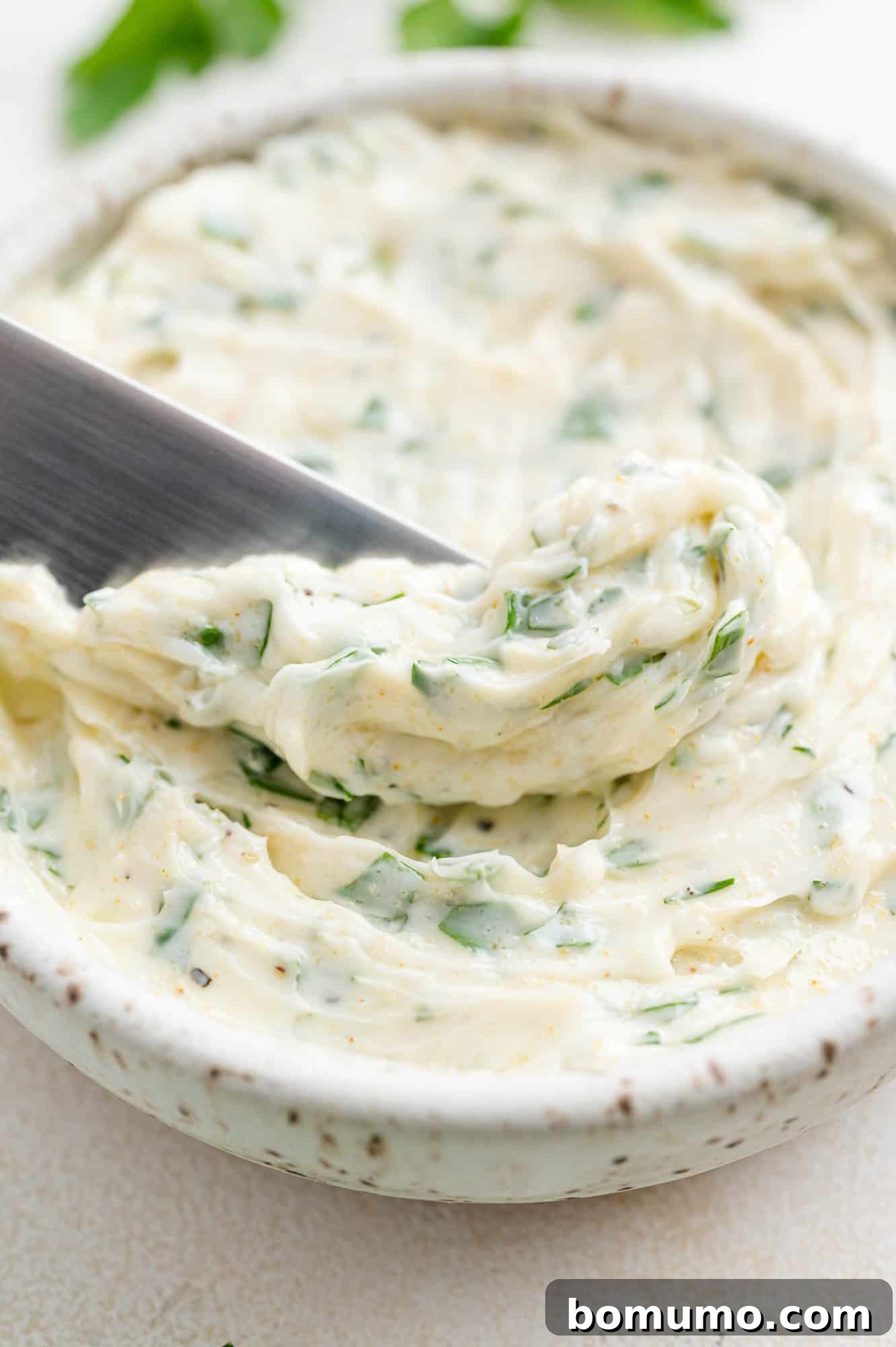 A bowl of freshly made garlic butter with a spreading knife on the side, ready to be used.
