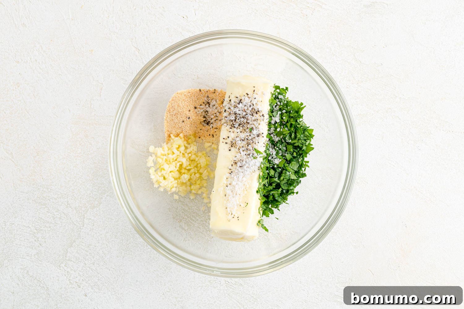Unmixed ingredients for garlic butter in a clear glass bowl, before combining.