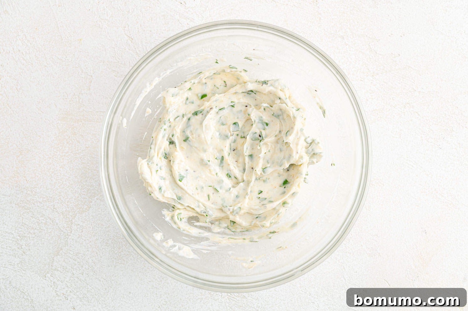 Garlic butter, perfectly mixed and homogenous, in a clear glass bowl.