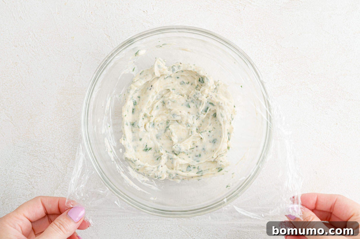 Plastic wrap being placed over a bowl of garlic butter for refrigeration, ensuring freshness.