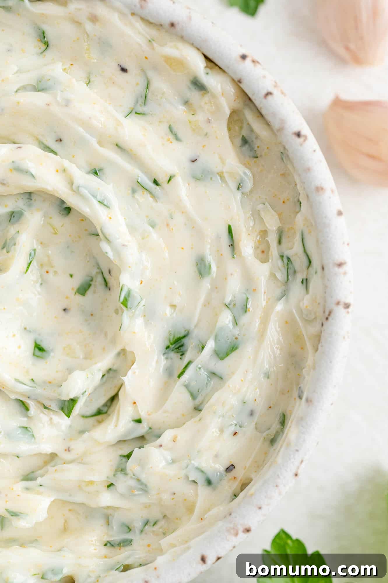 Close-up of creamy garlic butter in a speckled ceramic bowl, ready for use.