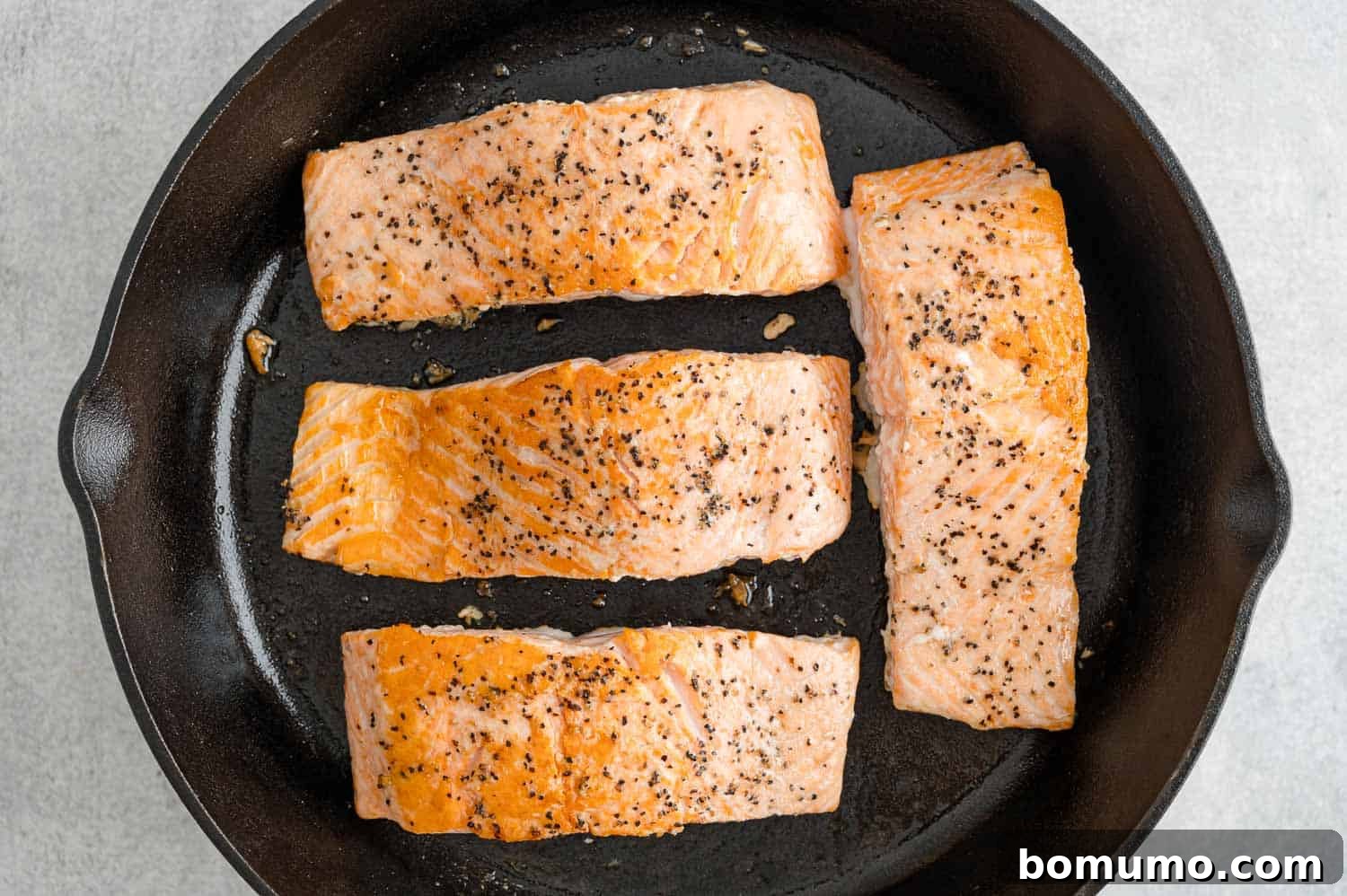 Four perfectly cooked, flaky salmon fillets resting in a black skillet, ready for their teriyaki glaze.