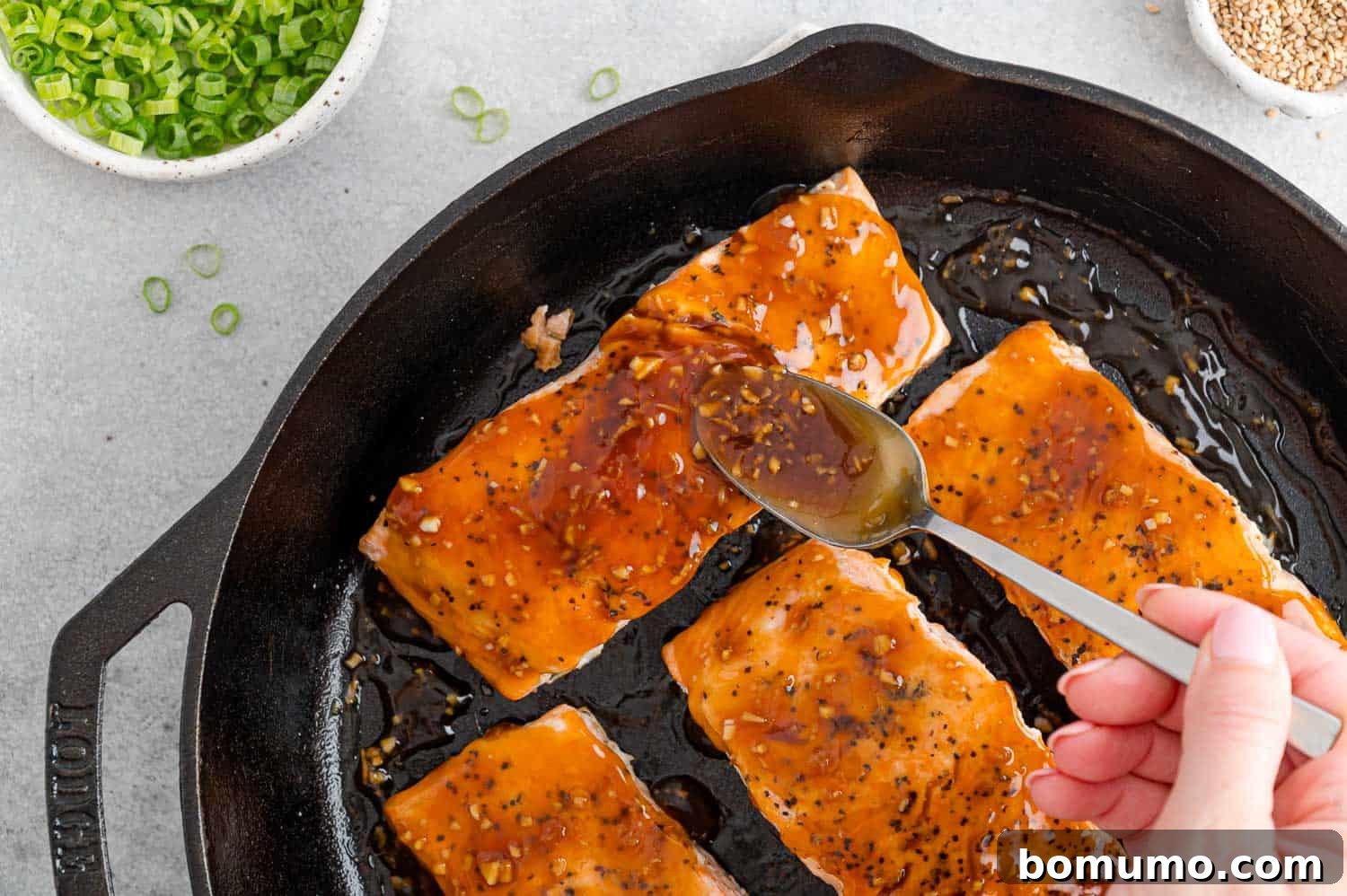 A ladle expertly spoons a rich, glossy teriyaki sauce over perfectly cooked salmon fillets, ready to be served.