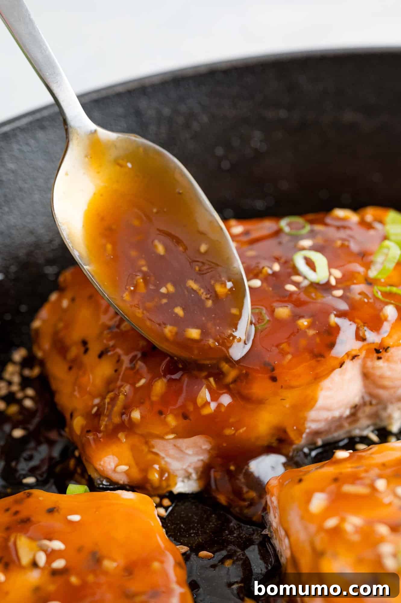 A generous spoonful of homemade teriyaki sauce being drizzled over a perfectly cooked salmon fillet, showcasing its glossy texture.