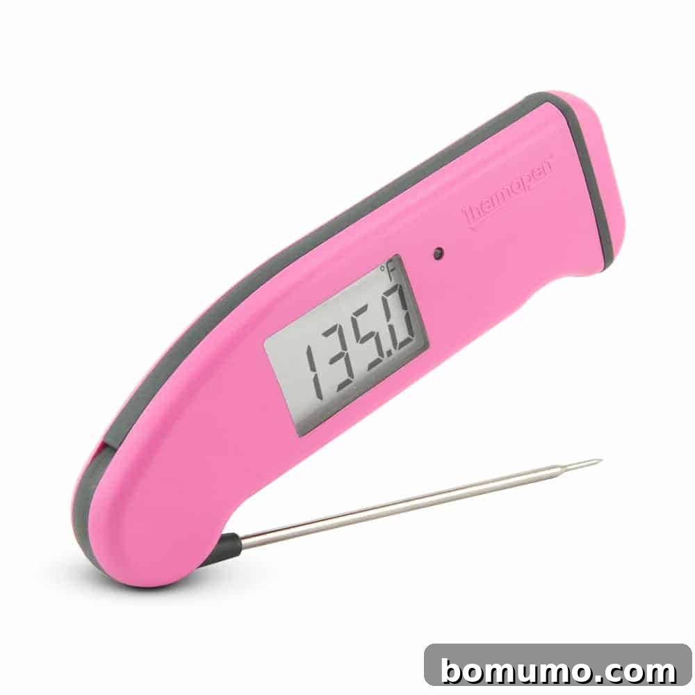 A pink instant-read thermometer resting on a white background, highlighting its precision for cooking.
