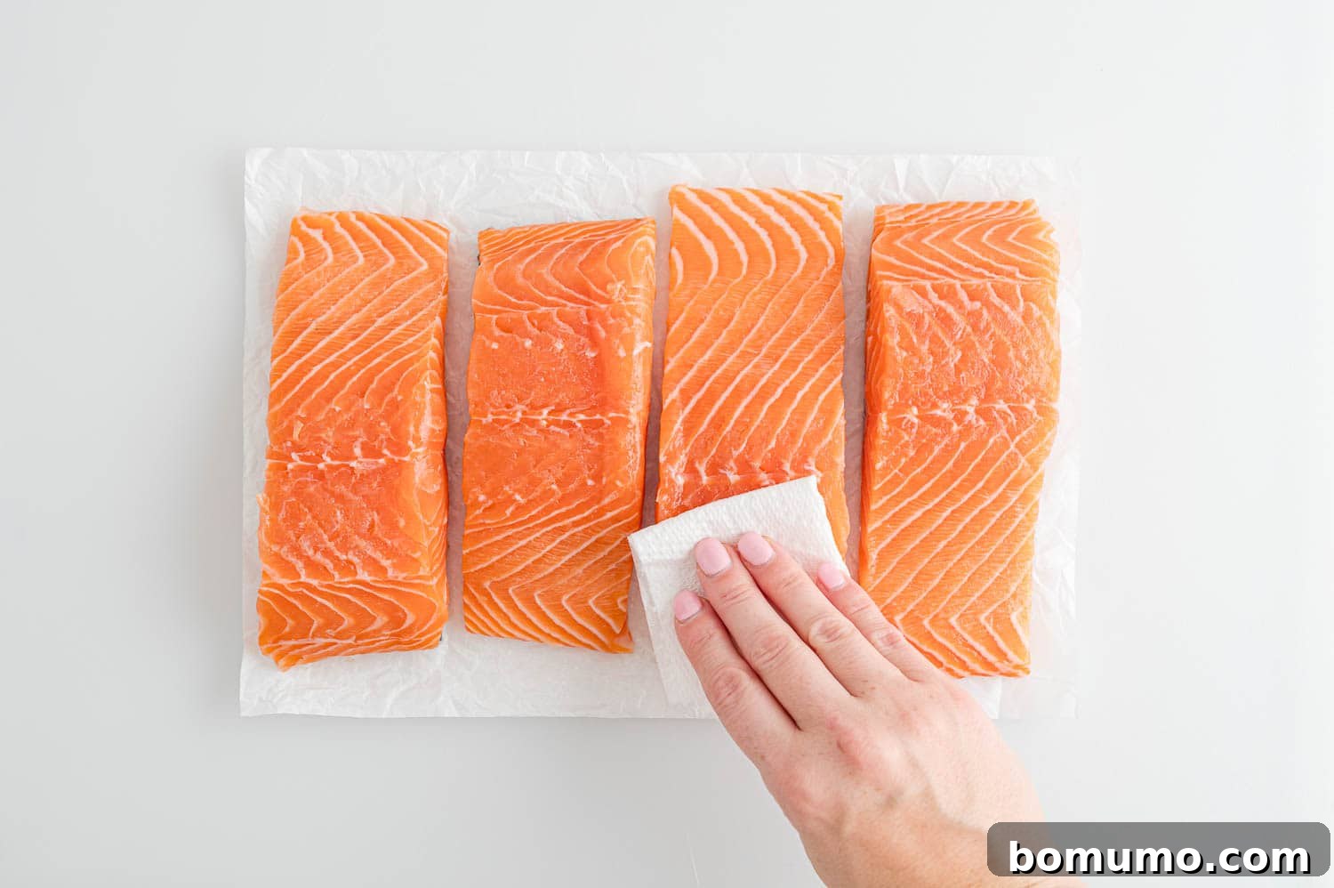Fresh salmon fillet being gently patted dry with a paper towel, preparing it for a perfect sear.