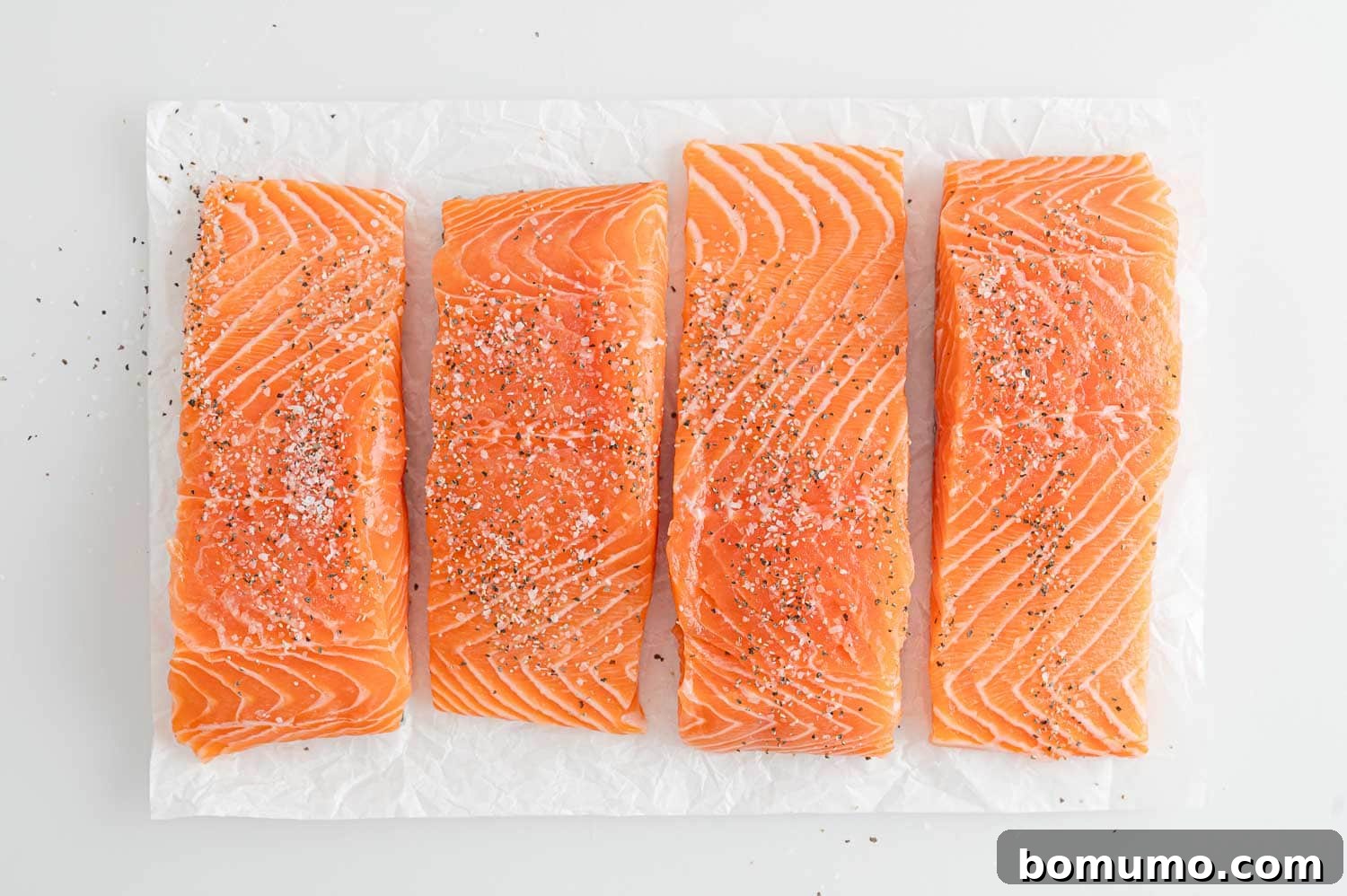 Salmon fillets meticulously seasoned with freshly ground salt and black pepper on a cutting board, ready for cooking.