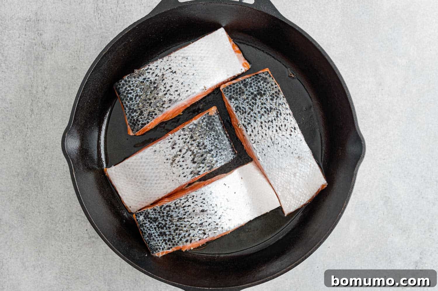 Salmon fillets searing in a hot frying pan, skin side up, creating a delicious crust.