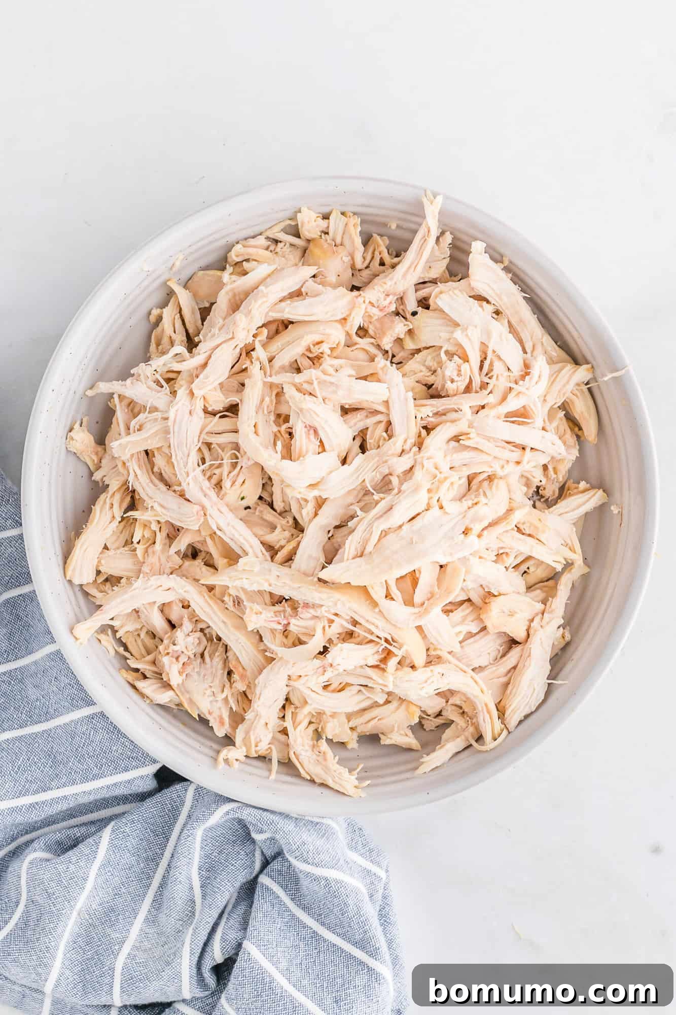 Shredded roasted bone-in chicken in a white bowl, ready for meal prep or serving.