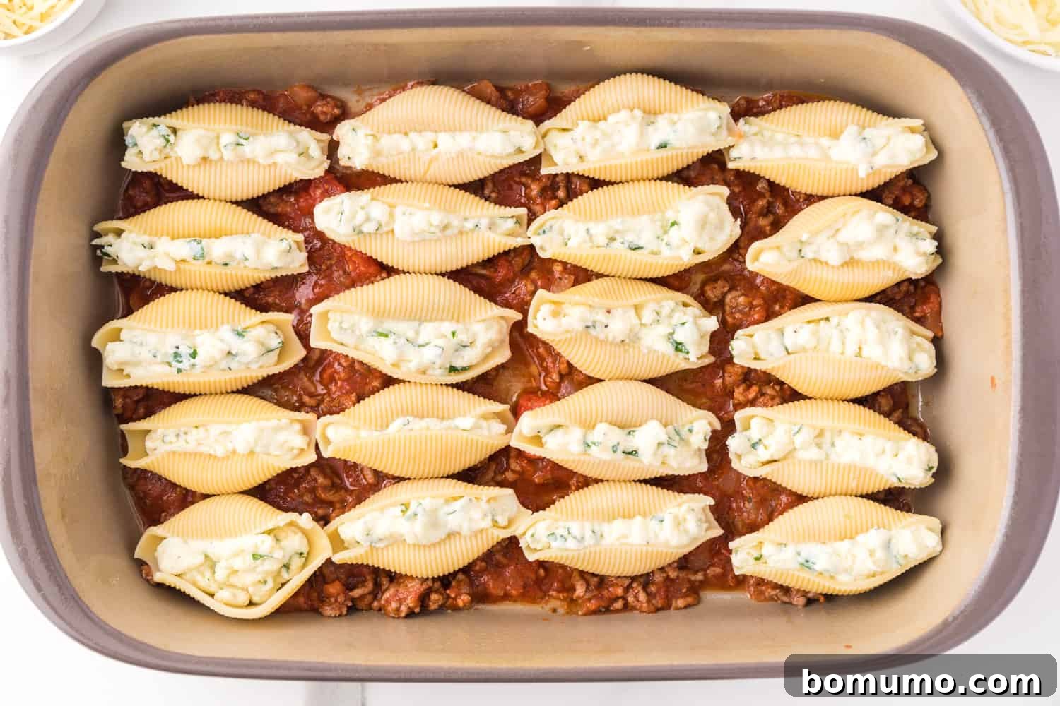 Savory Meat-Filled Jumbo Shells 11 Neatly arranged, cheese-stuffed pasta shells settled on a layer of rich meat sauce in a baking dish, perfectly positioned for the next steps.