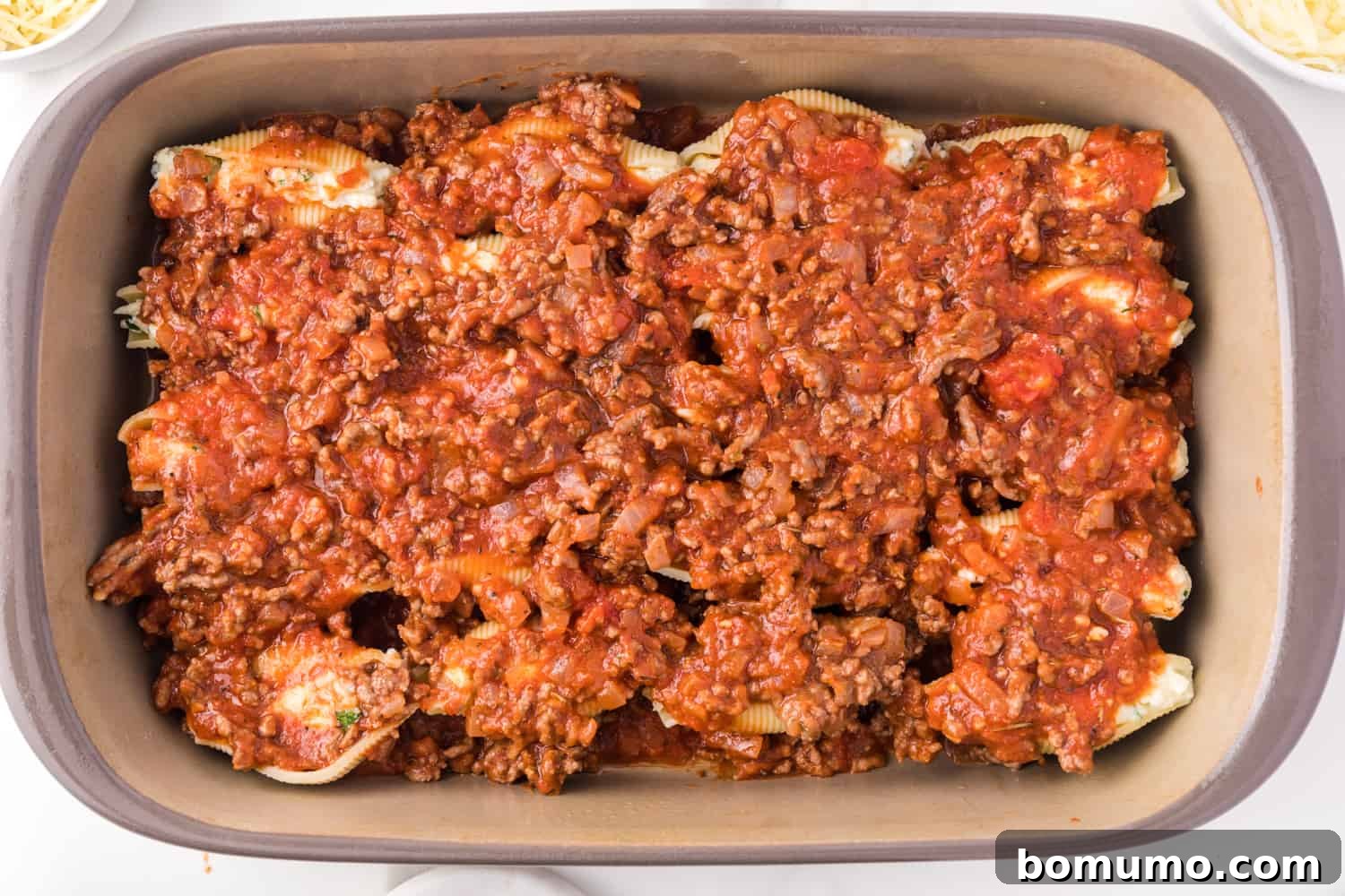 Savory Meat-Filled Jumbo Shells 12 Rich meat sauce being poured generously over a layer of stuffed pasta shells in a baking dish, ensuring every shell is covered in savory goodness.