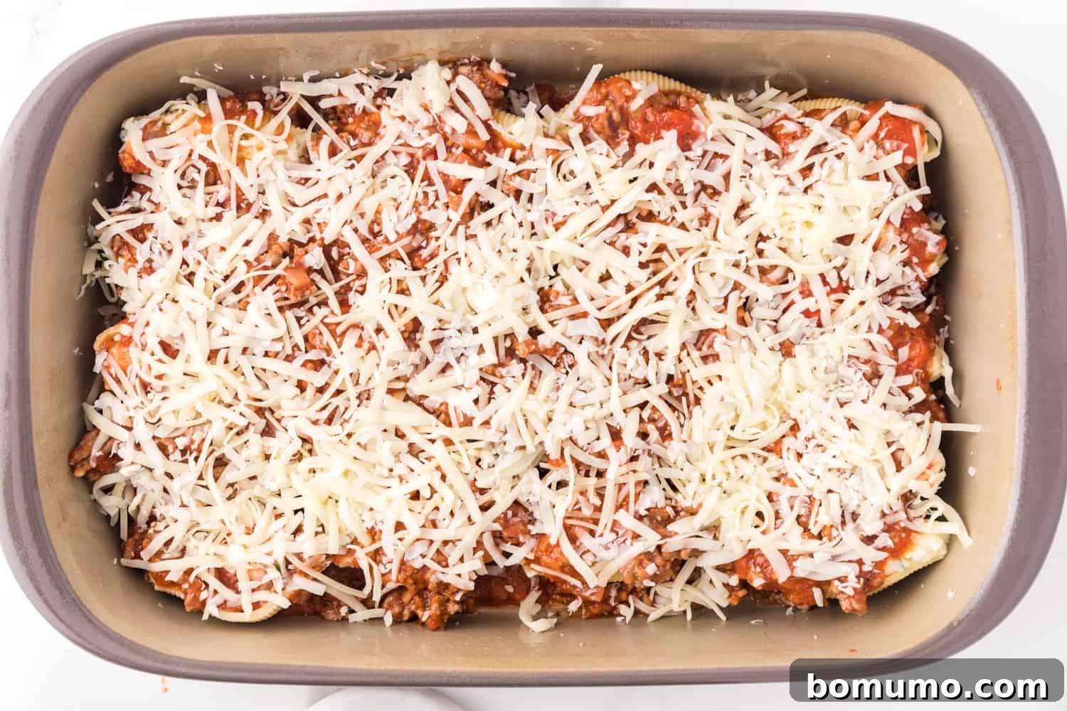 Savory Meat-Filled Jumbo Shells 13 The fully assembled casserole of stuffed shells, generously topped with shredded mozzarella and Parmesan cheese, gleaming and ready for the oven.