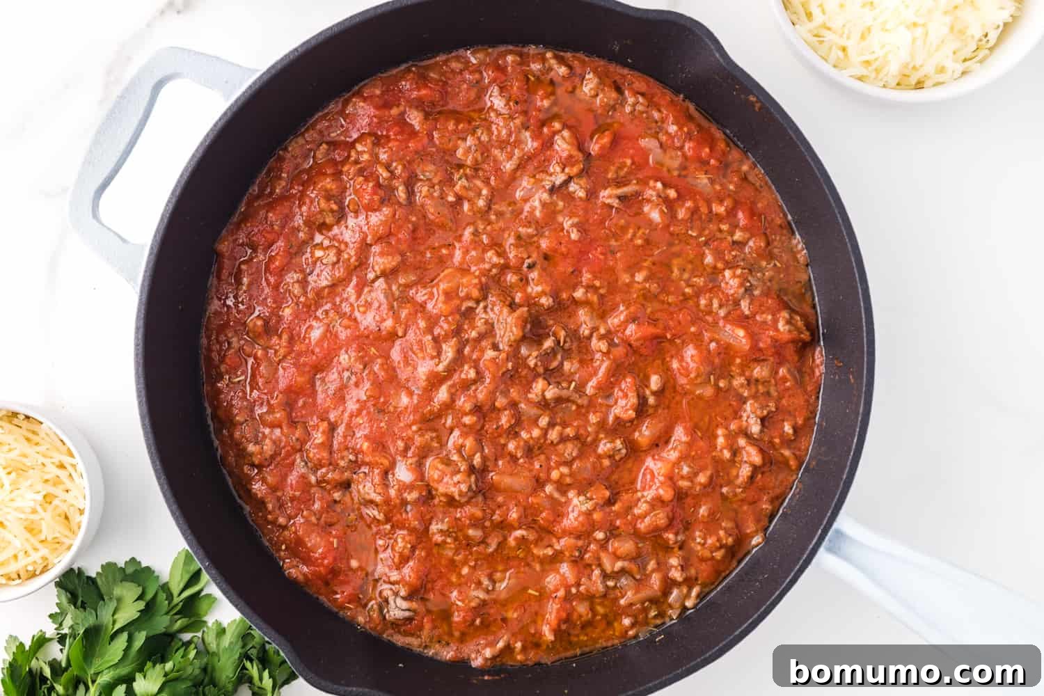 Savory Meat-Filled Jumbo Shells 7 A vibrant red pasta sauce being poured into a skillet with browned ground beef and onions, ready to be combined for a rich meat sauce.