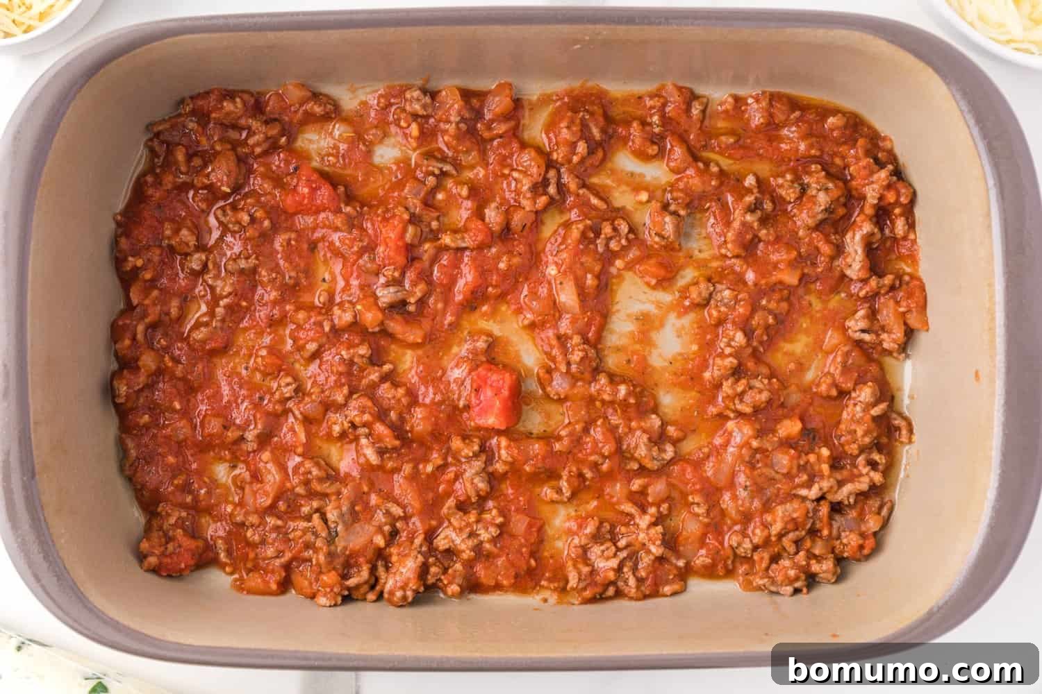 Savory Meat-Filled Jumbo Shells 10 A vibrant layer of rich meat sauce spread evenly across the bottom of a 9x13 inch baking pan, creating the base for the stuffed shells.