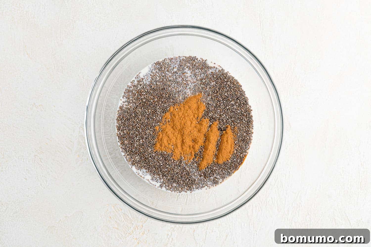 All liquid and dry ingredients, unmixed, in a clear glass bowl.