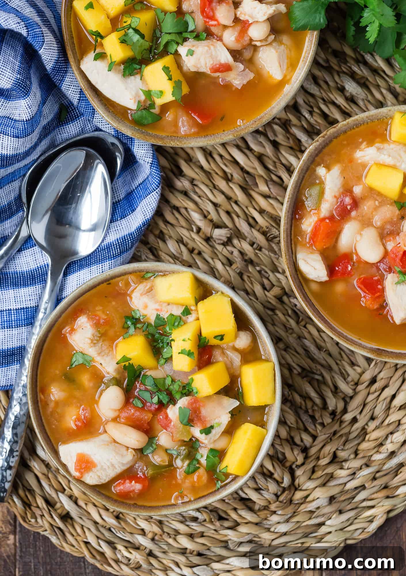 Overhead view of three bowls of hearty and flavorful Jerk Chicken Chili, garnished with fresh cilantro and diced mango.