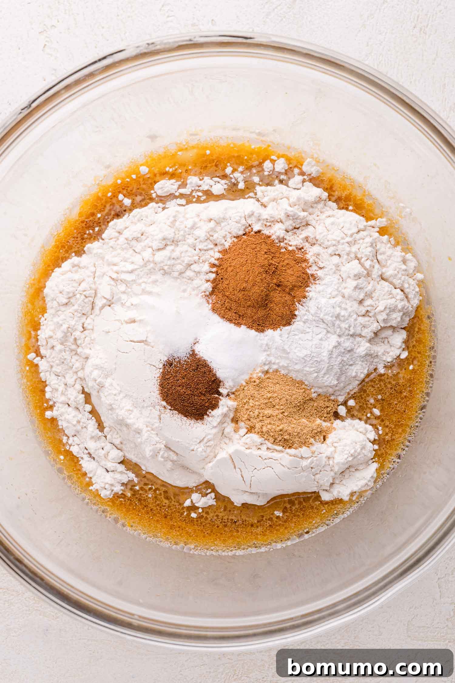 Gingerbread Bliss Pancakes 6 A glass bowl containing flour, baking powder, and ground spices on top of a wet ingredient mixture, ready to be mixed.