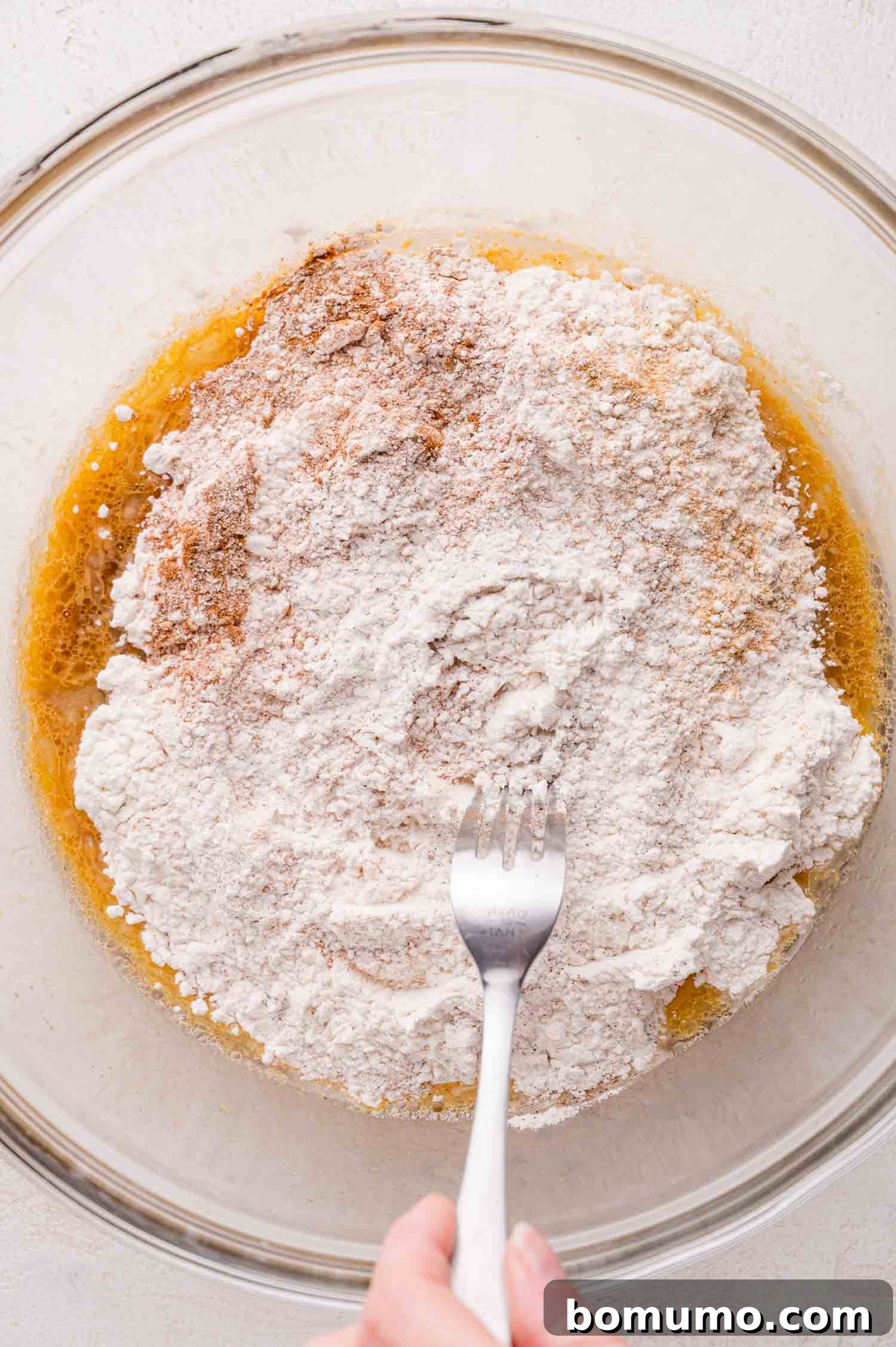 Gingerbread Bliss Pancakes 7 A hand holding a fork is mixing flour and spices into a bowl with wet ingredients.