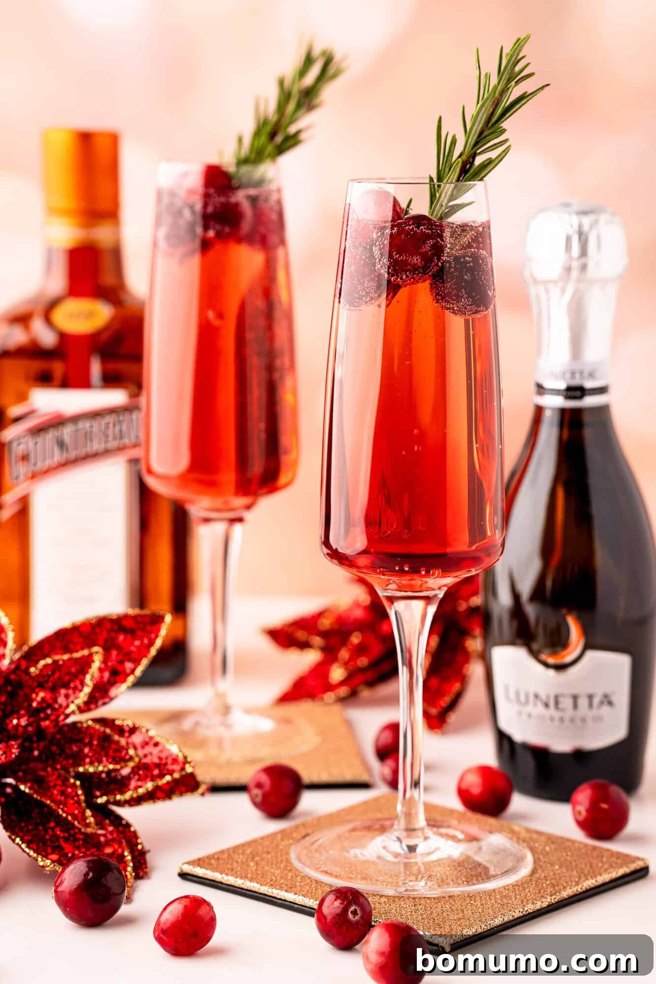 Festive Poinsettia Cocktails served in champagne flutes with cranberry and rosemary garnish, alongside Cointreau and Prosecco bottles.