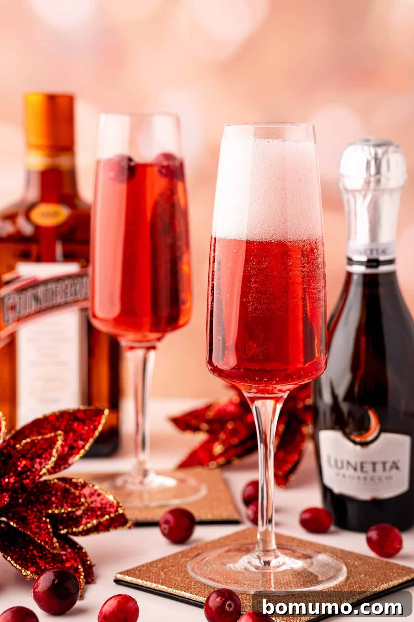 Two champagne flutes with red sparkling cocktails, garnished with cranberries.