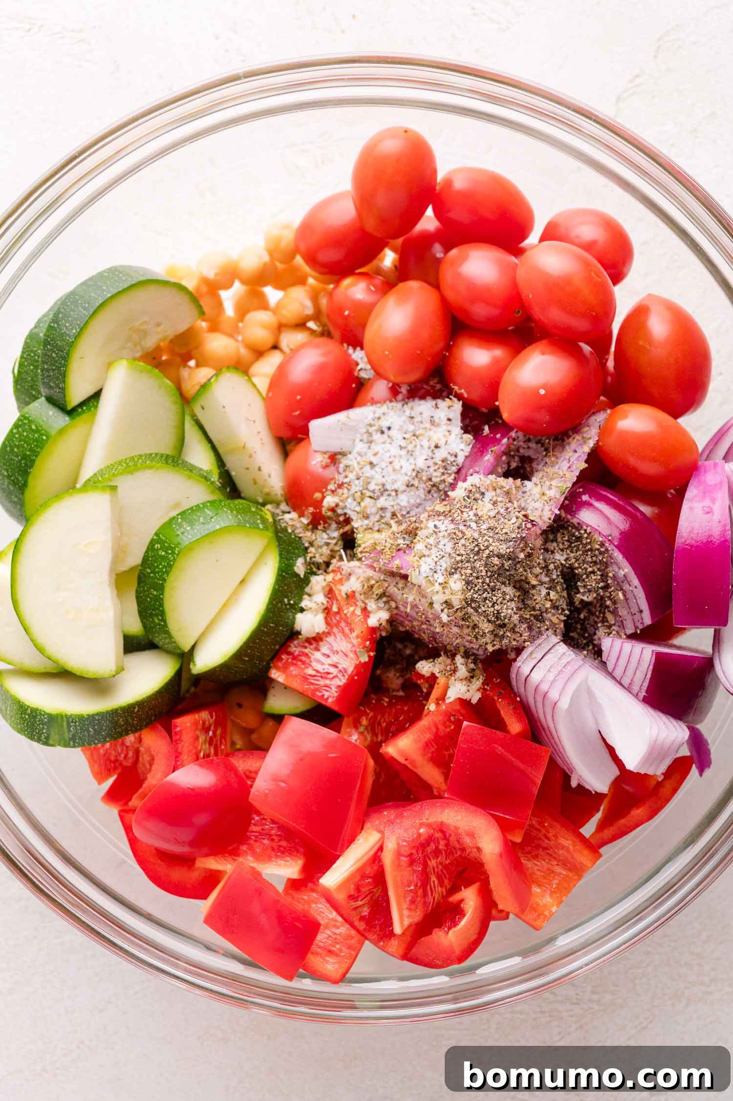 Vegetables and chickpeas in a glass bowl with seasonings.