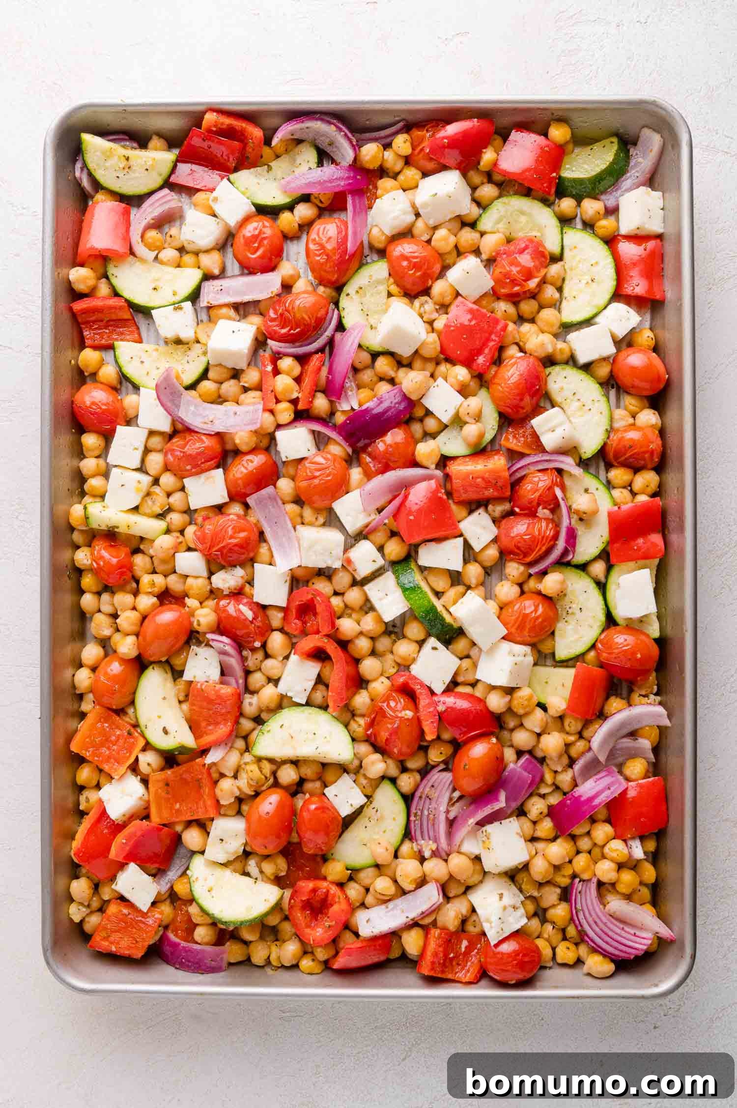 Chopped vegetables, chickpeas, and halloumi cheese arranged on a baking sheet.