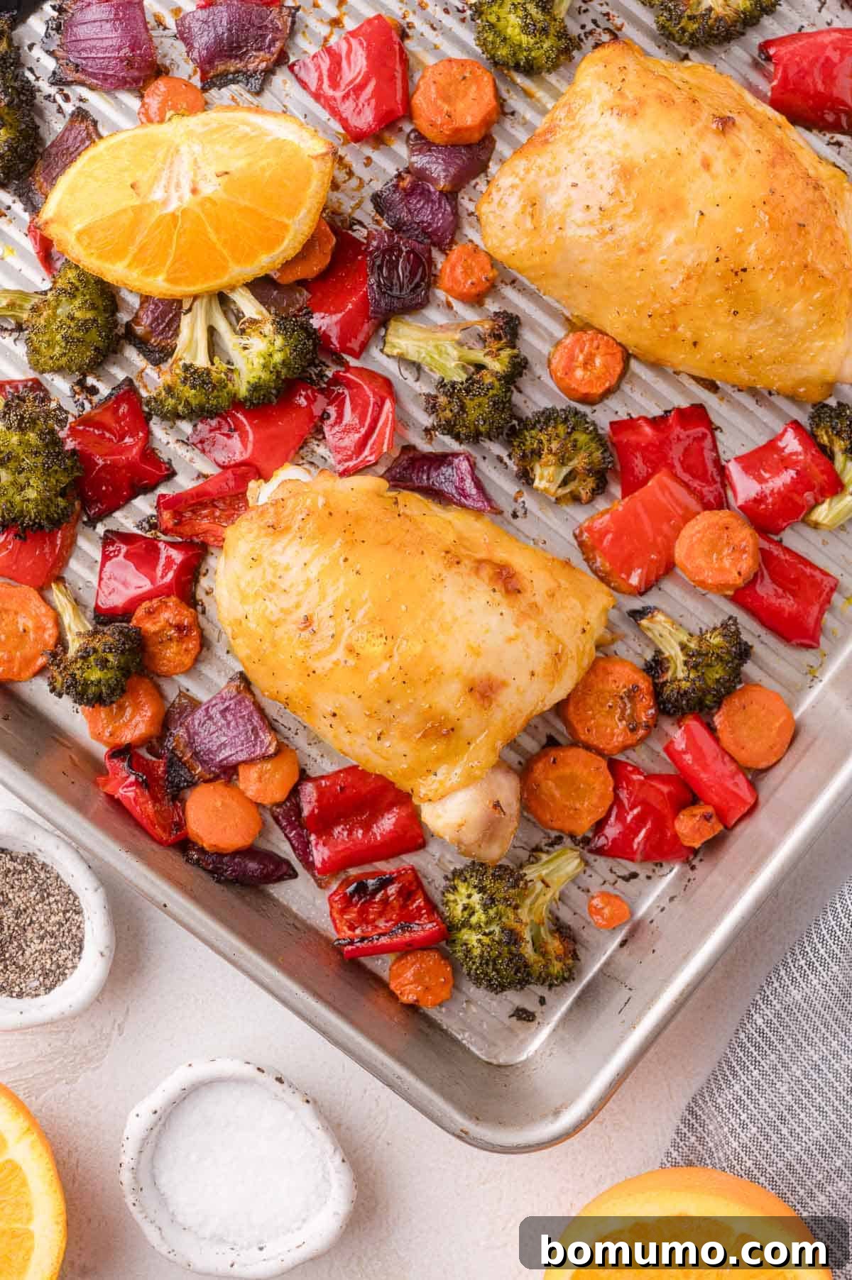Sheet Pan Citrus Chicken and Rainbow Vegetables: Chicken thighs baked with broccoli, carrots, red bell pepper, red onion, and orange slices, seasoned with salt and pepper.